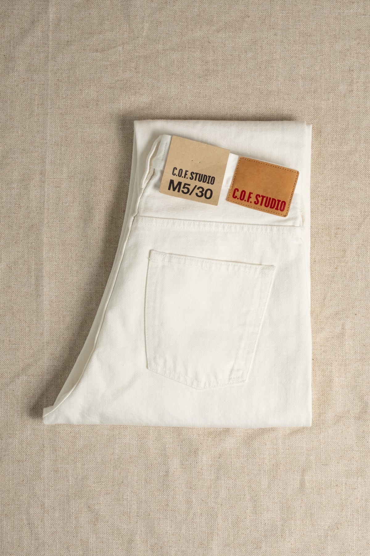White jeans with a brand label on a beige fabric background